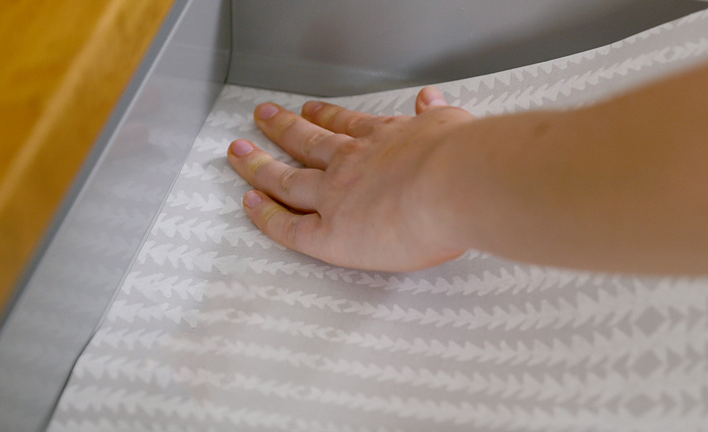 A person uses peel and stick wallpaper to line a drawer.