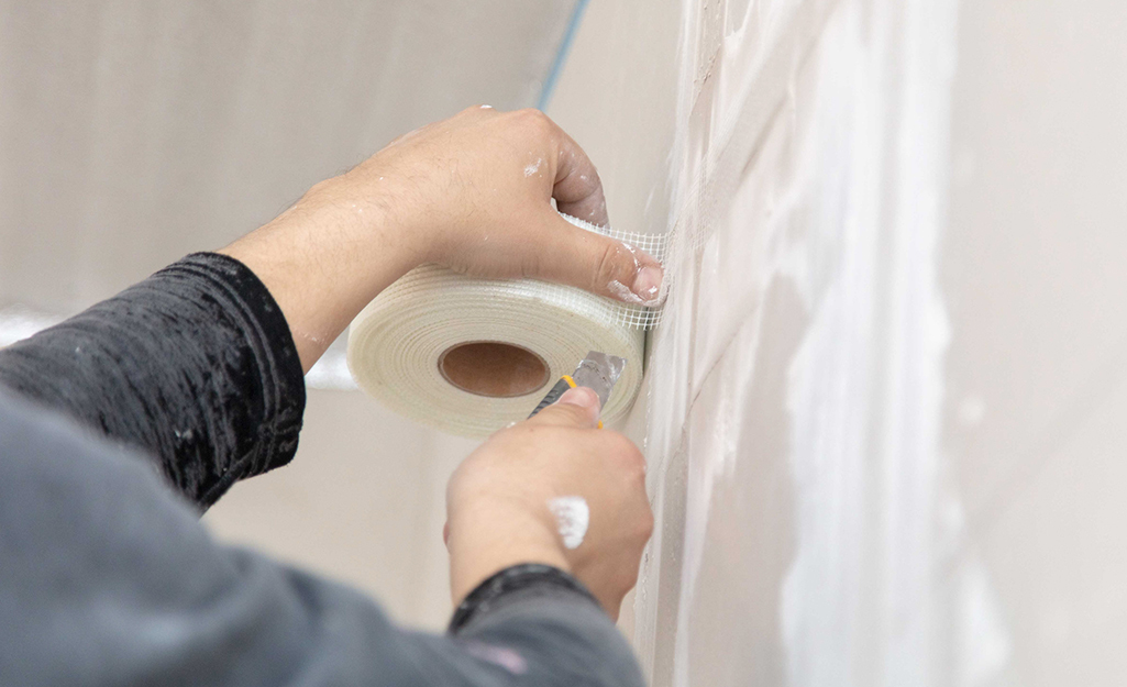 A worker places fiberglass mesh tape to a mudded drywall joint.