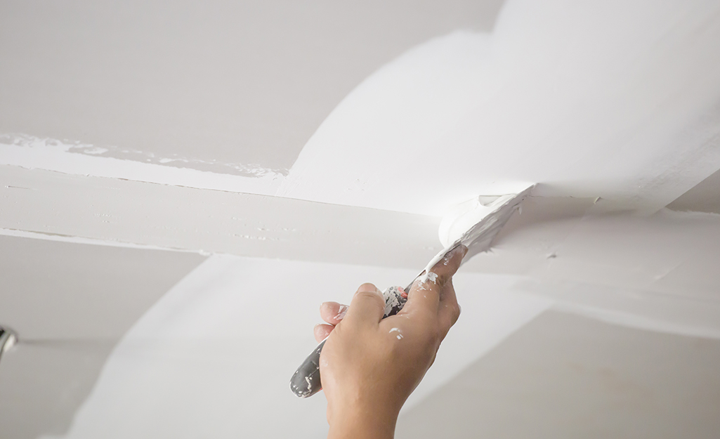 A worker applies a second coat of drywall mud to a joint.