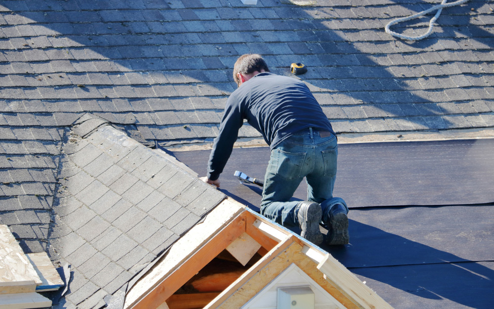A man securing a tarp to a section of a roof
