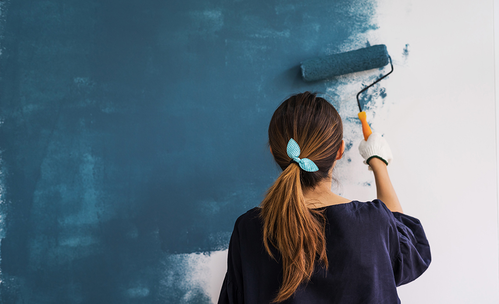 A woman paints a wall blue using a paint roller.