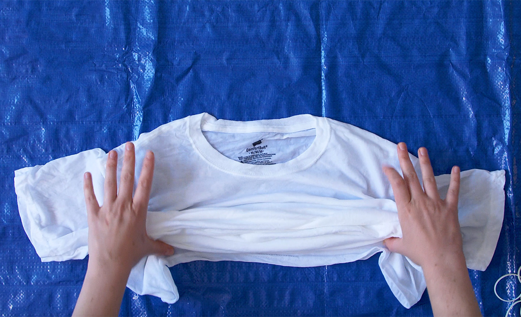 A woman lies a white t-shirt on a tarp. 