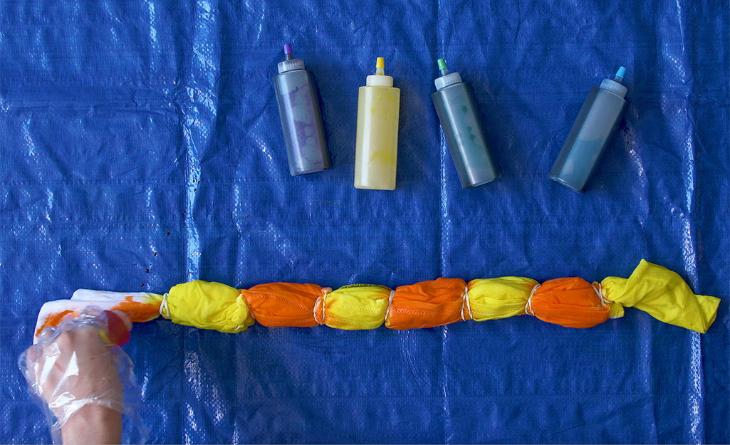 A person squeezes orange dye on a shirt wrapped in rubber bands. 