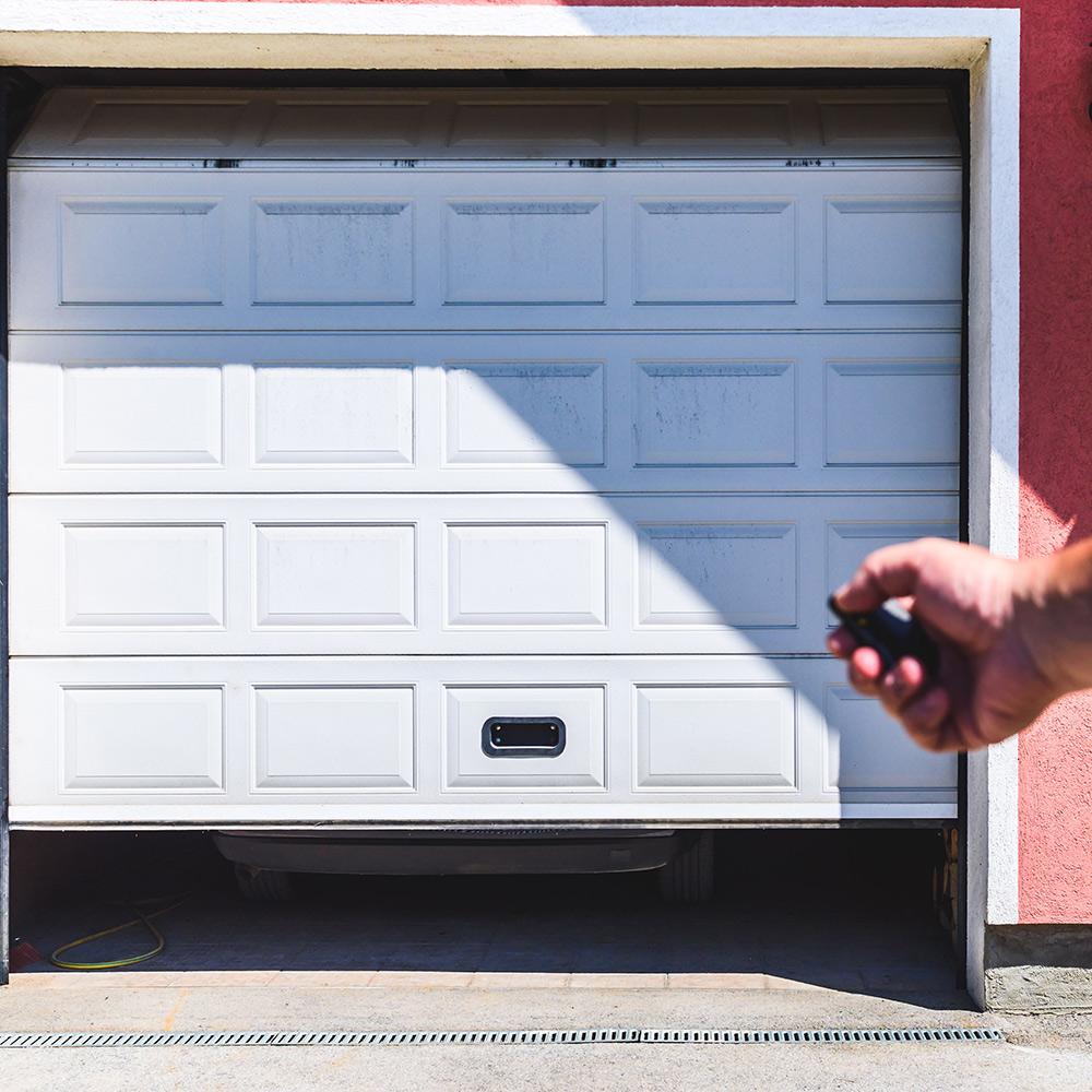 A person uses a remote control to open a garage door.