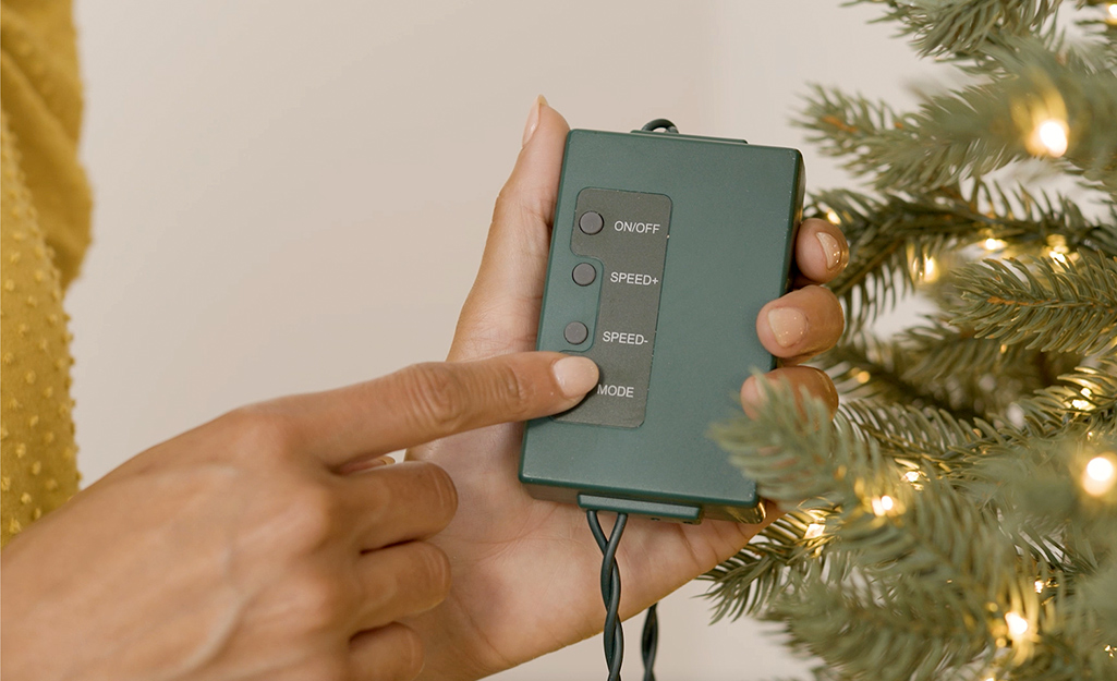 A person presses the mode button on a controller for Christmas tree lights.
