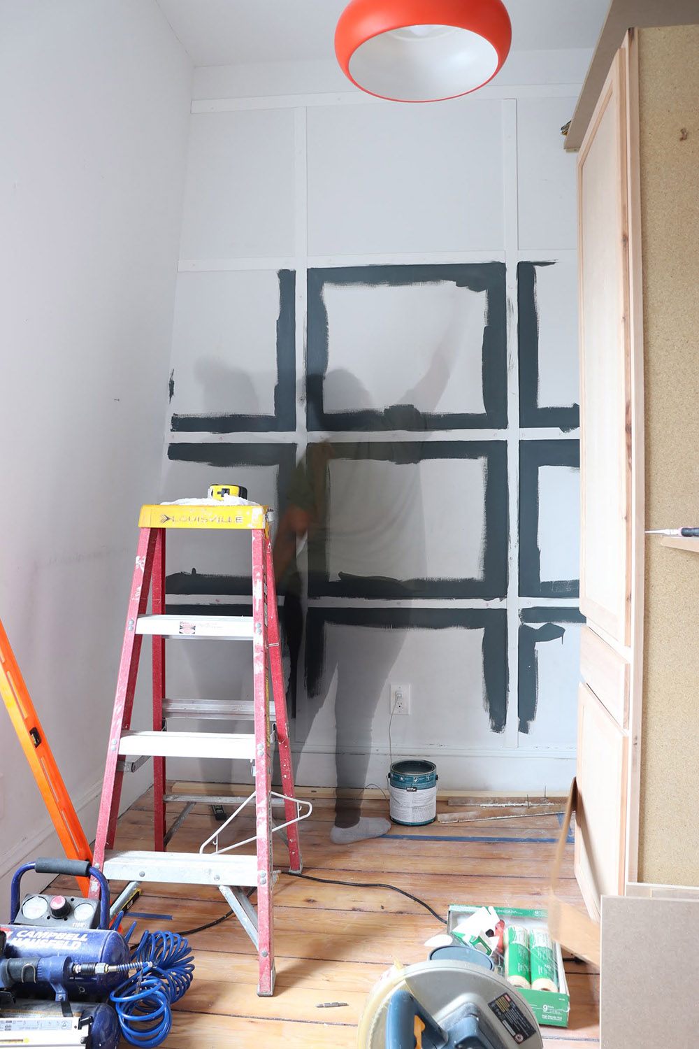 A grid wall being pained using paint and a ladder
