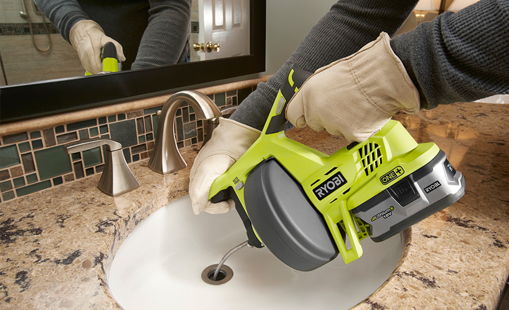 a person using a drain snake to unclog a sink