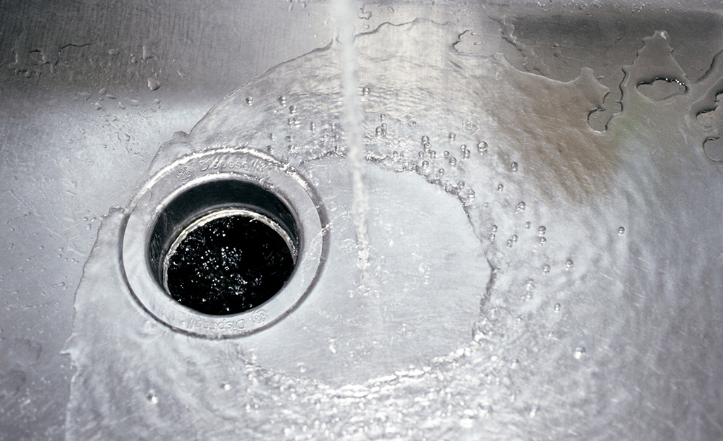Water running into the garbage disposal in a stainless steel sink basin.