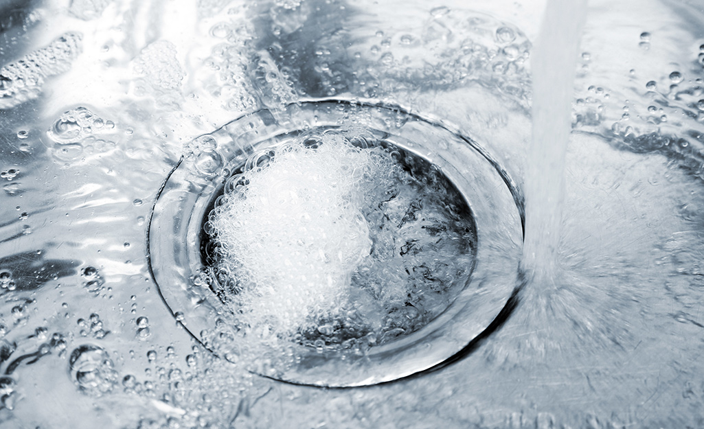 A person uses boiling water to unclog a kitchen sink.