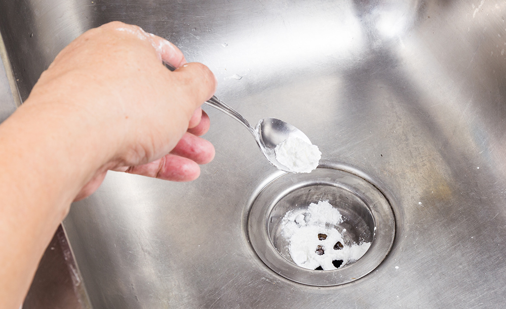 A person uses baking soda to unclog a kitchen sink.