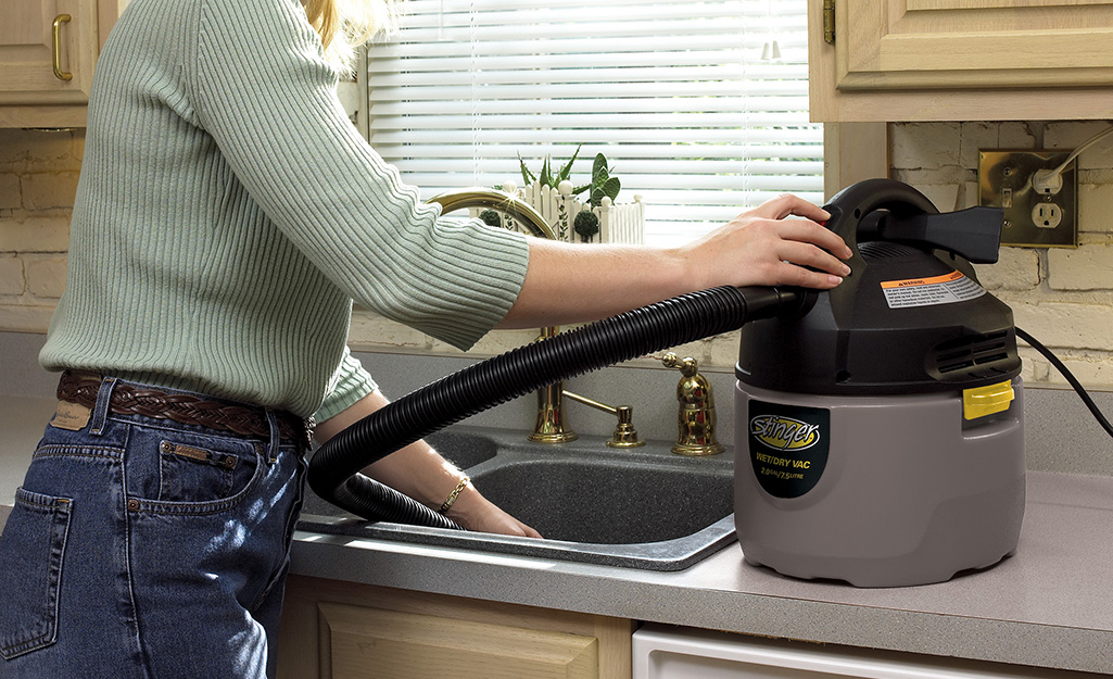 A person uses a wet-dry vacuum to unclog a kitchen sink.