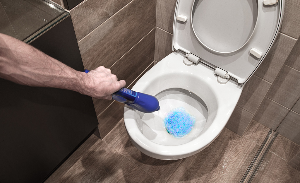 Une personne qui verse du savon à vaisselle liquide dans une cuvette de toilette.