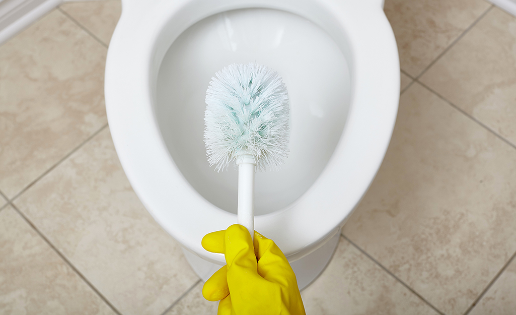 A person wearing rubber gloves holding a toilet brush above a toilet bowl.