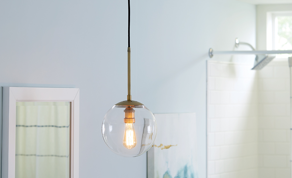 A pendant light with a clear glass globe hangs from the ceiling of a bathroom.