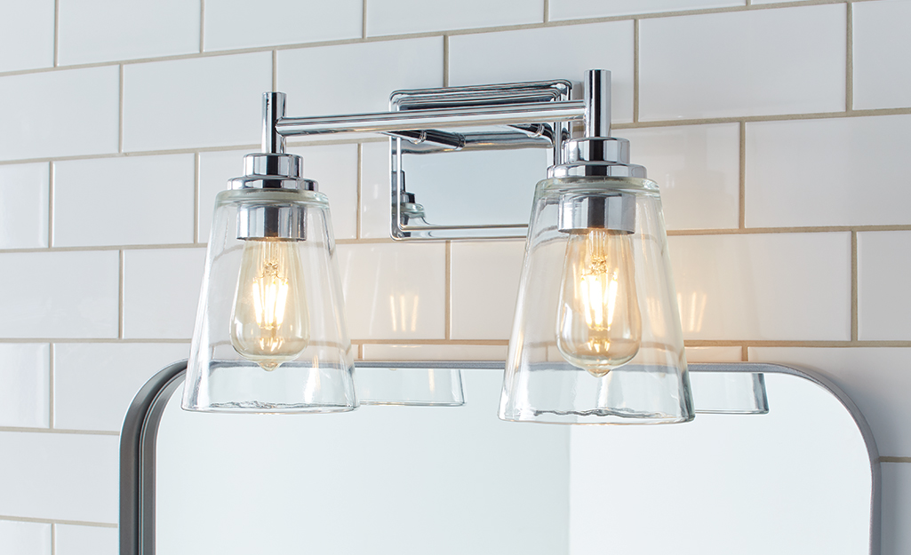 A vanity light bar with two fixtures that have glass shades hangs above a mirror in a bathroom.