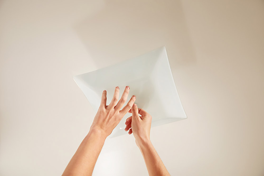 A person removes a cover from a ceiling mounted light fixture.