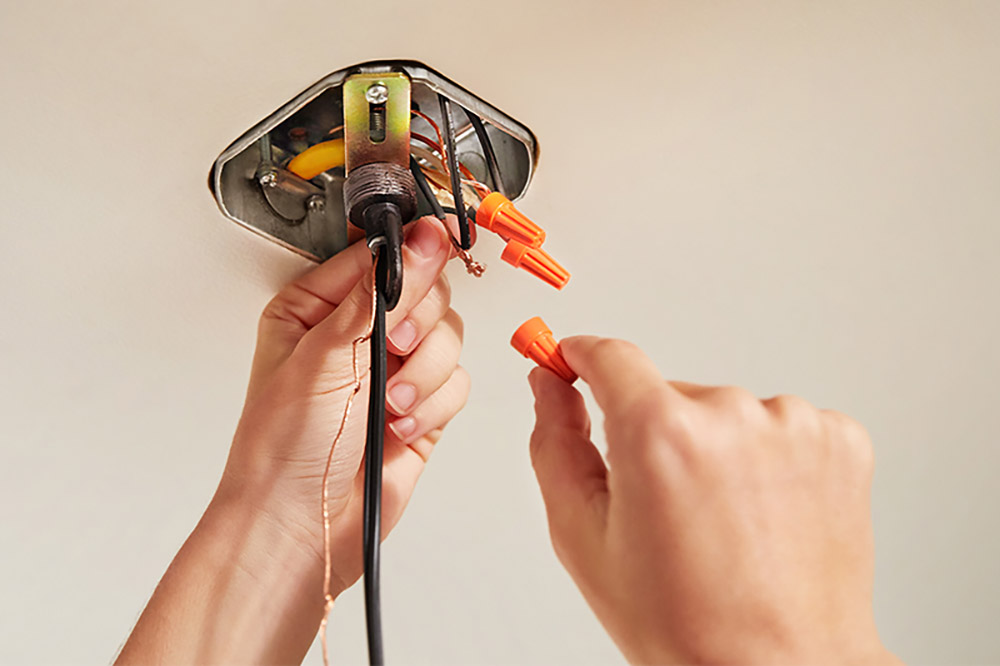 A person holding a black wire in one hand and an orange wire nut in the other hand. 