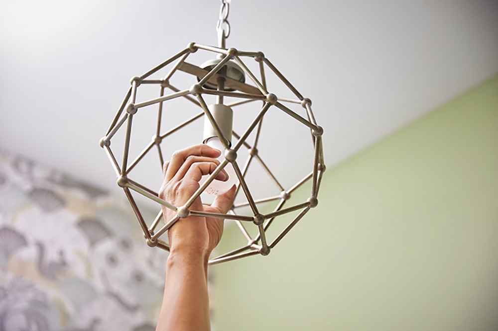 A person screws in a light bulb on a new hanging bathroom light fixture.