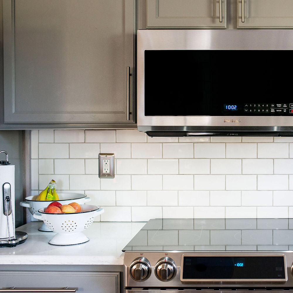 A stainless steel microwave hangs above a white tile backsplash and an oven range.