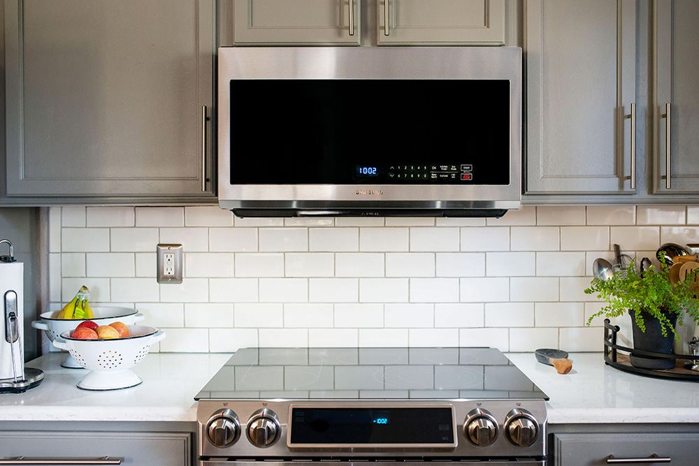 A kitchen with a slide-in oven range in front of a white tile backsplash.