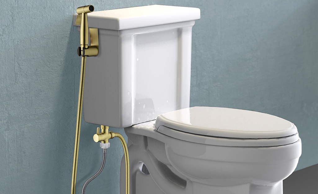A bidet with a hand-held sprayer installed on the side of a toilet in a bathroom.