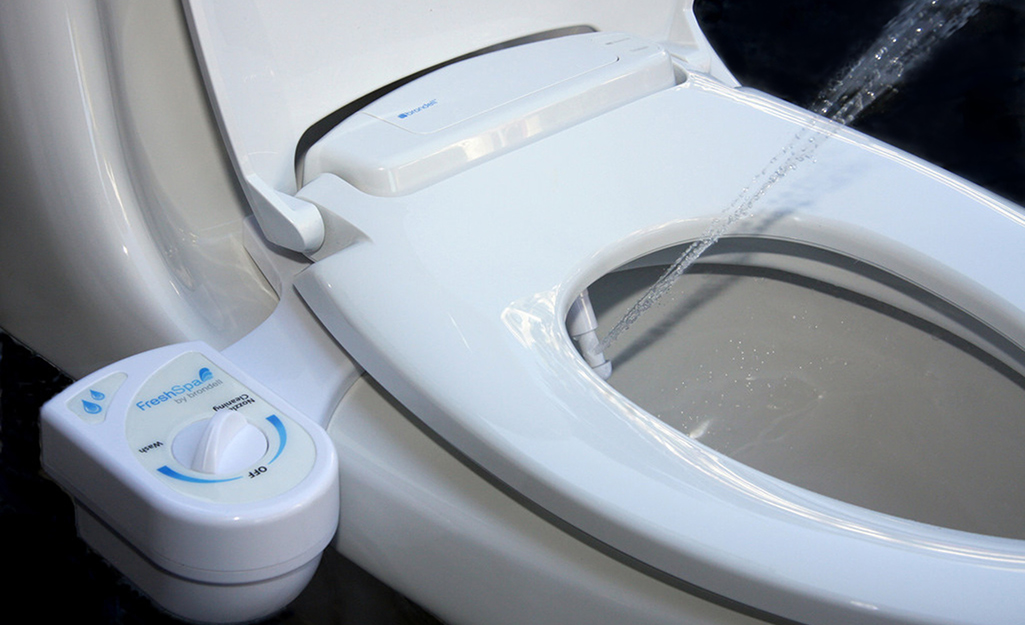 A toilet seat bidet sprays water from a nozzle.