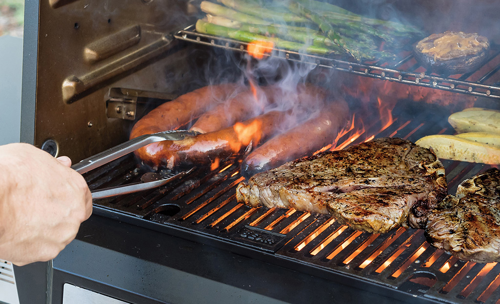 A person cooks meats and vegetables on a barbecue grill.