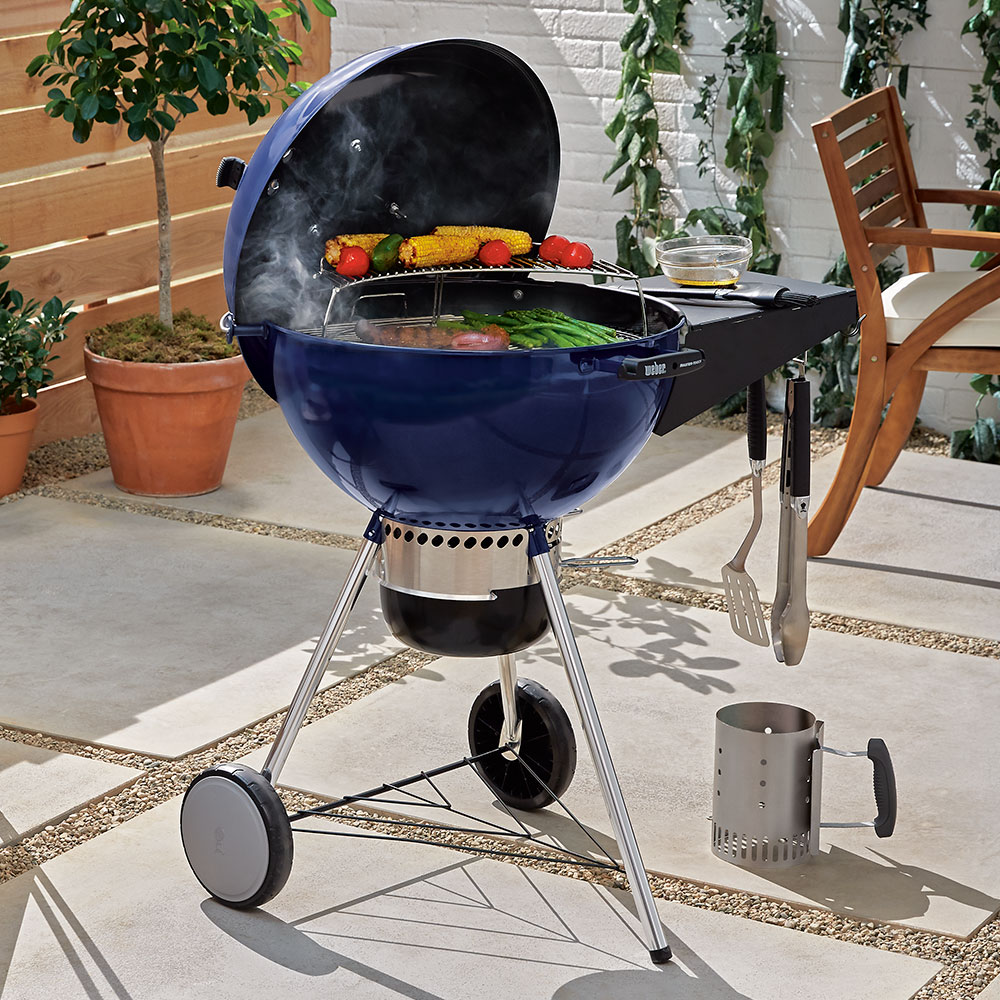 A blue kettle grill cooking food on a patio.