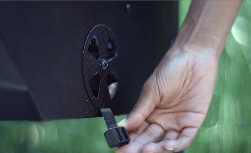 A person adjusting the lower vent on a charcoal grill. A person adjusting the lower vent on a charcoal grill.