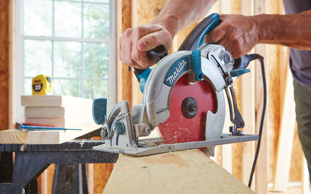 Person sawing a board with a circular saw. 