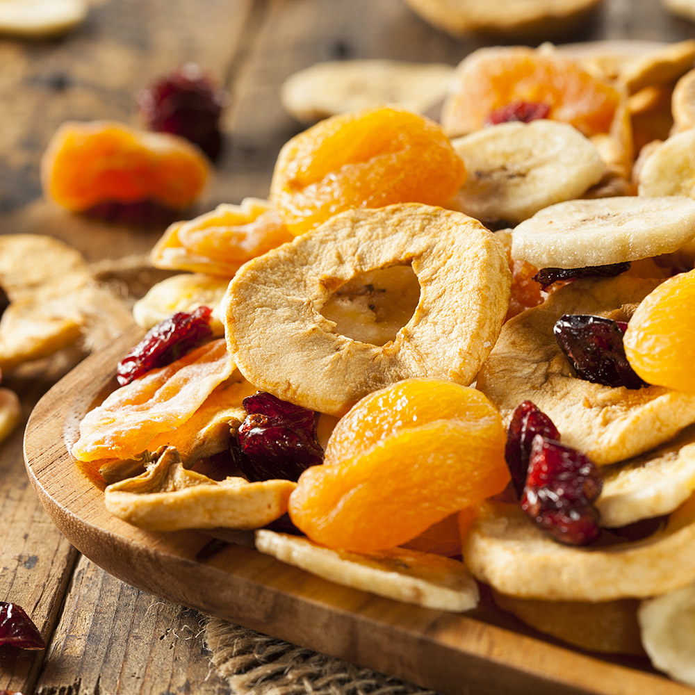 A wooden bowl of dried fruit sitting on a wood table.