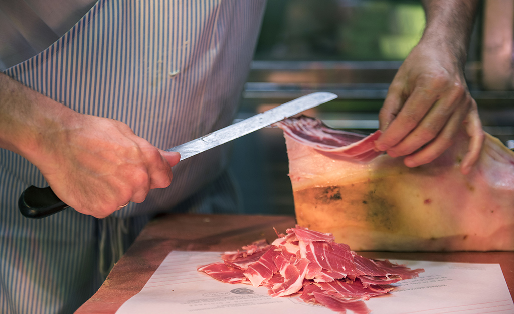 Man cutting thin slices of ham with a knife.