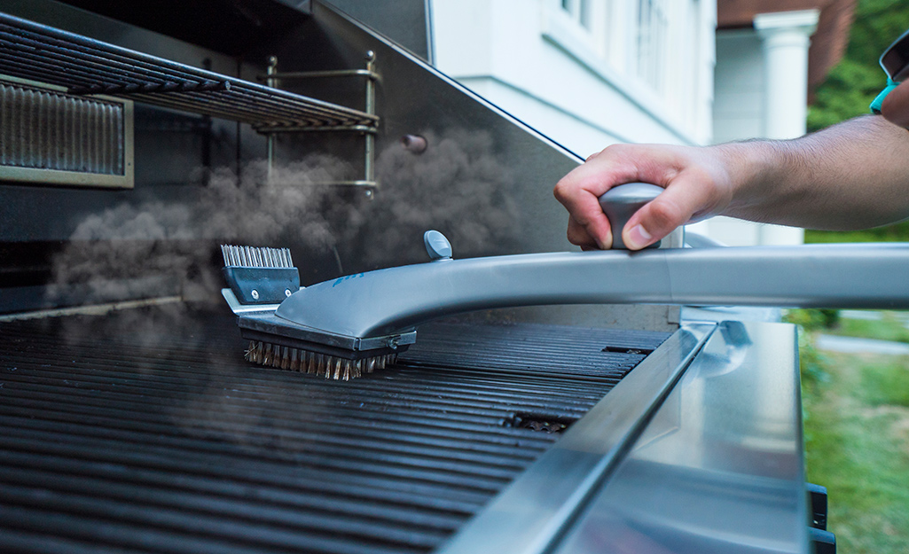 A person using a wire grill brush to clean a cooking grate.