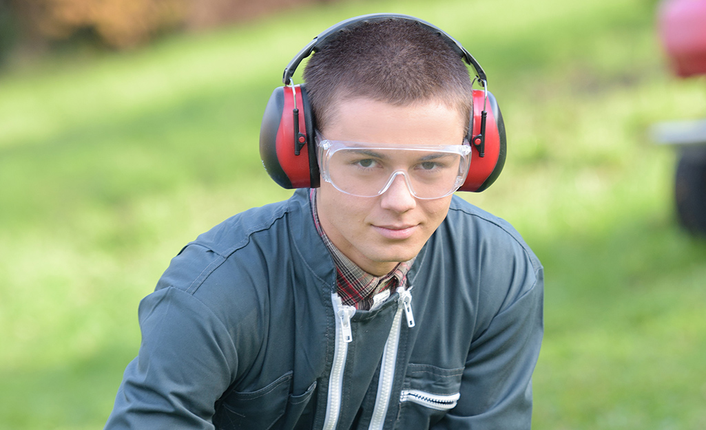 Man wearing red ear muffs to protect ears from loud leaf blower noises. 