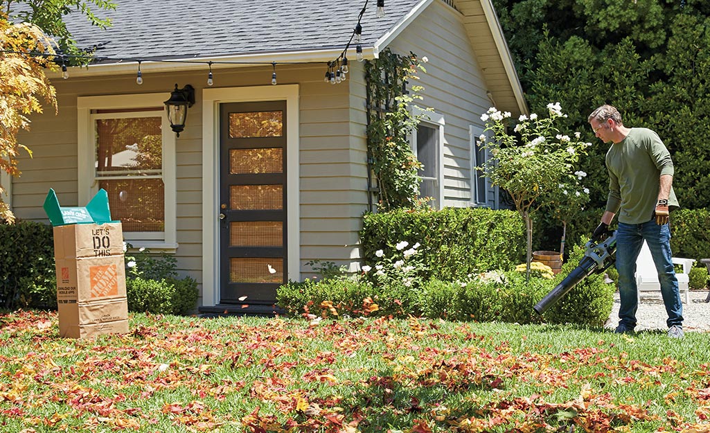 Man blowing leaves in a yard with a leaf blower with a lawn bag in yard. 