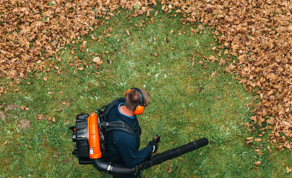 Man operating a leaf blower on his back and wearing protective ear muffs. 