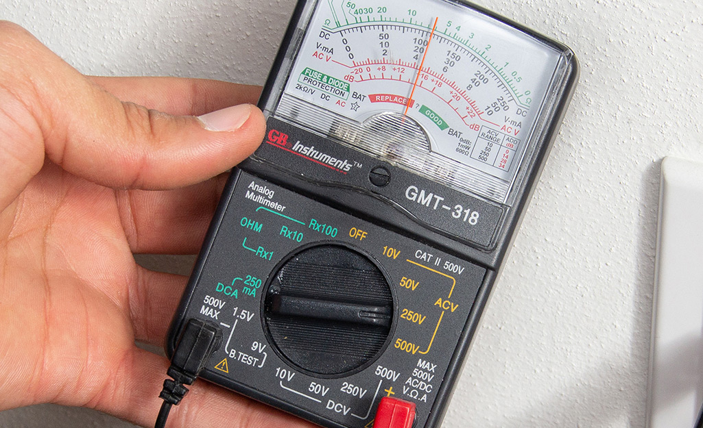 Someone holds an analog multimeter.
