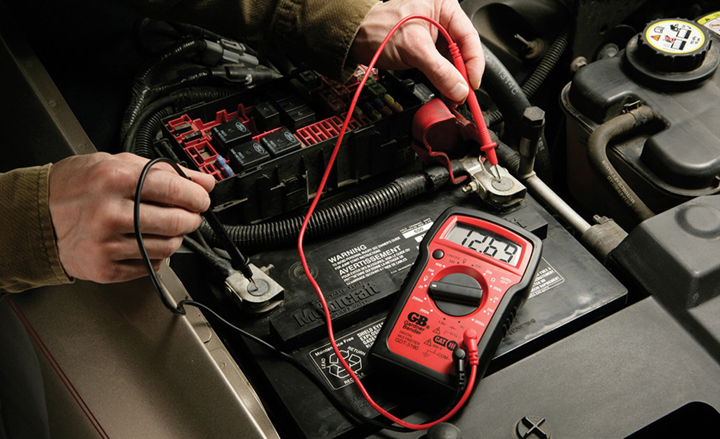 Someone testing a car battery with a digital multimeter.
