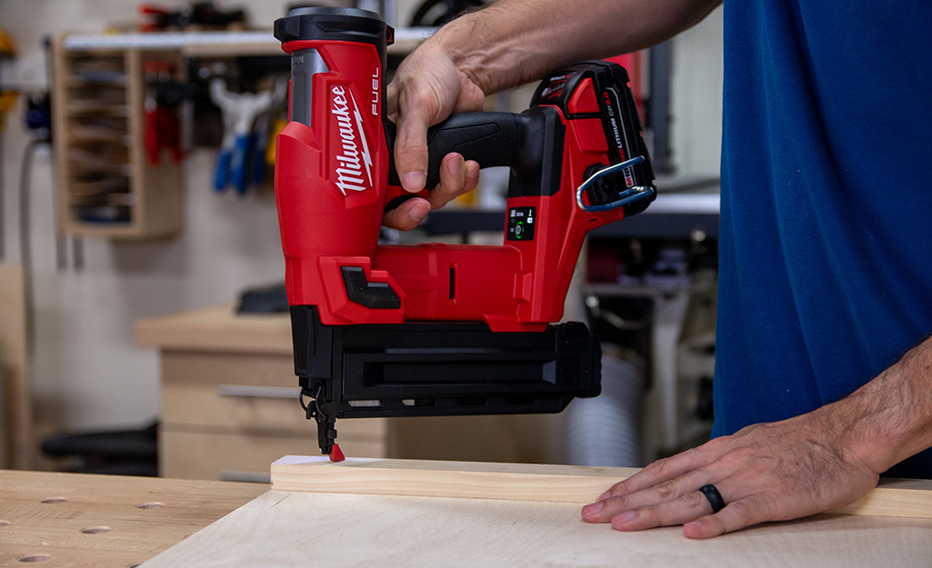 A person using a red nail gun on a piece of wood.