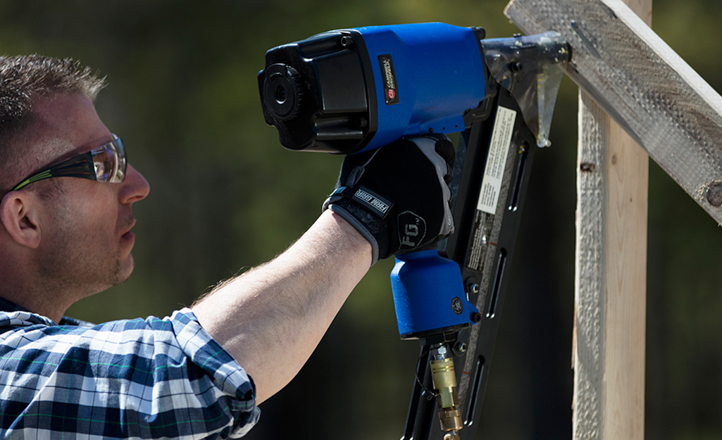 A person wearing protective glasses and gloves while using a blue nail gun.