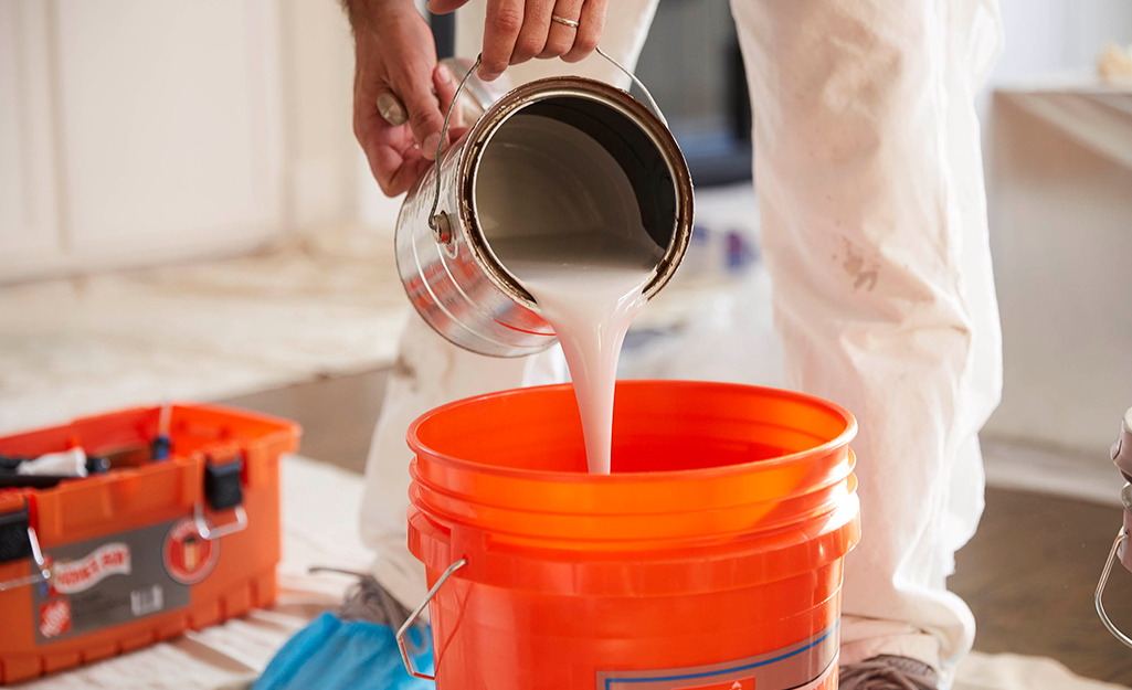 A person pours paint into a bucket for mixing.