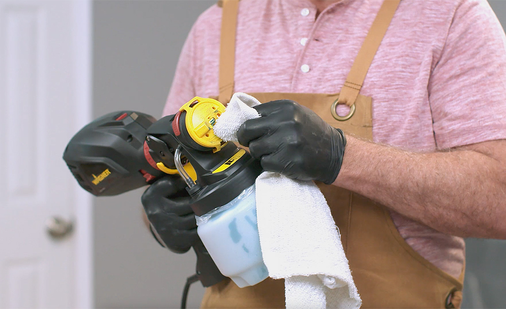 A person uses a cloth to clean a paint sprayer.