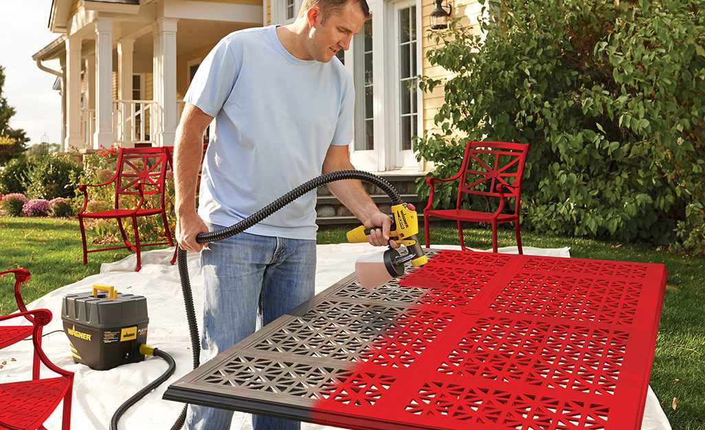 A person uses an HPLV sprayer to apply red paint on a table. 