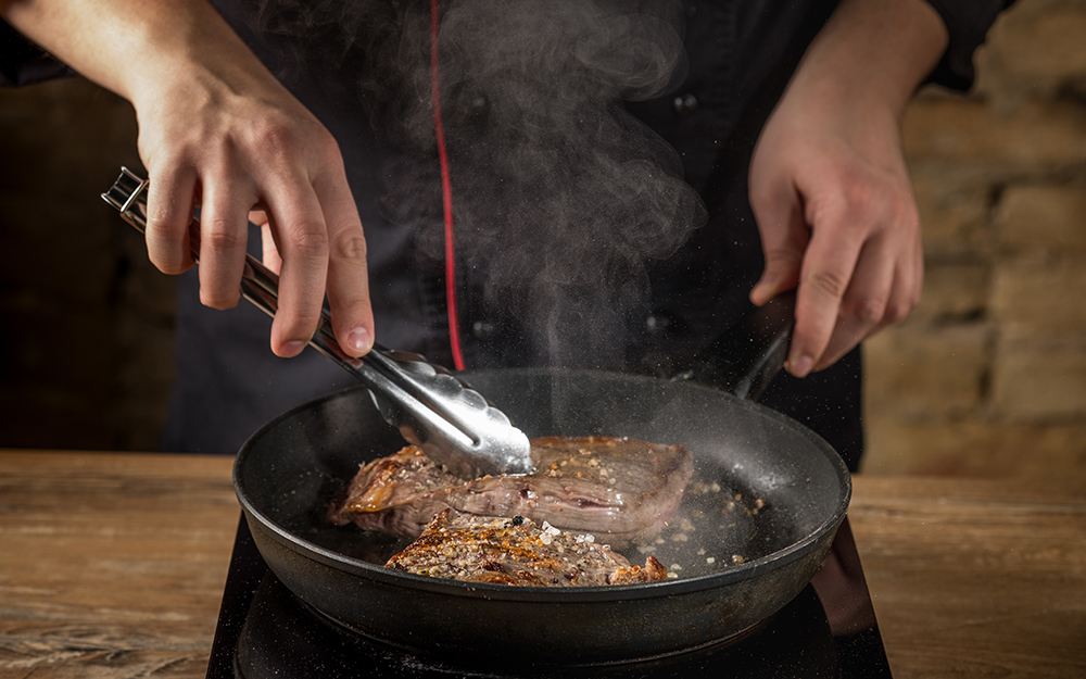 A person browning meat in a pan.