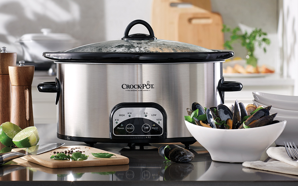 A slow cooker stands on a counter alongside cooked mussels.
