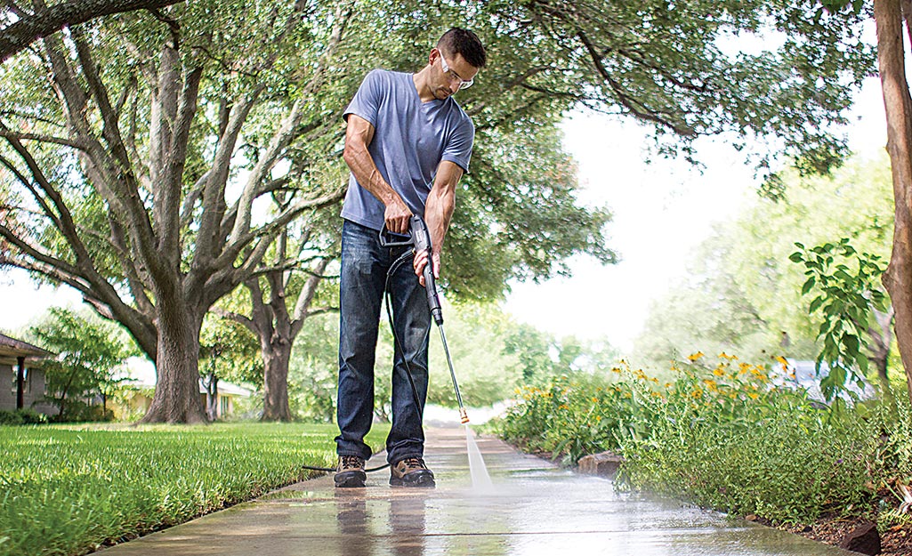 A man wears safety goggles to pressure wash his sidewalk. A man wears safety goggles to pressure wash his sidewalk.