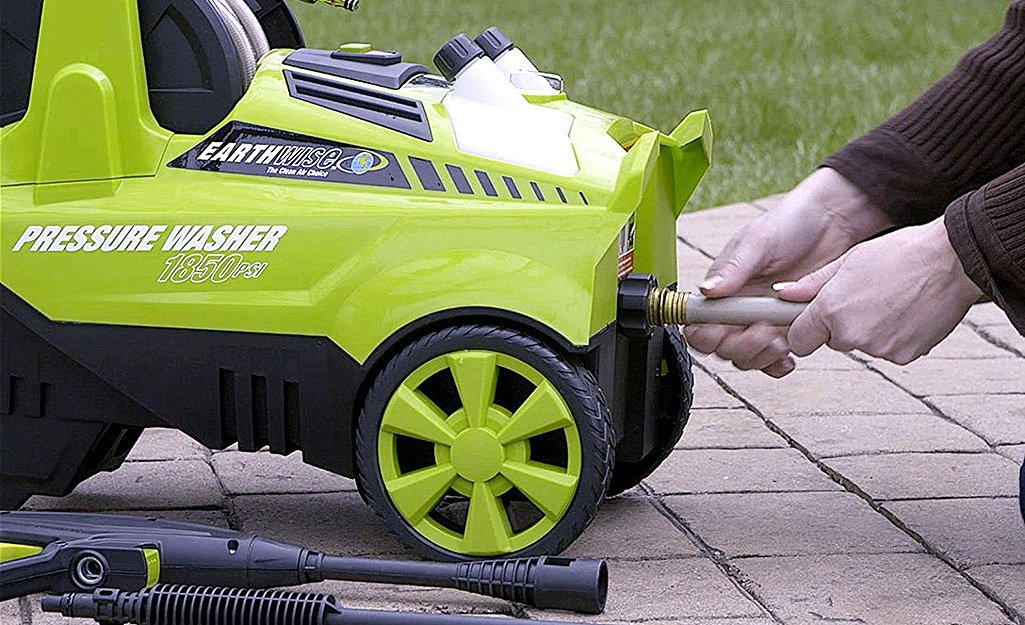 A person removes a garden hose from the pressure washer's water inlet. 
