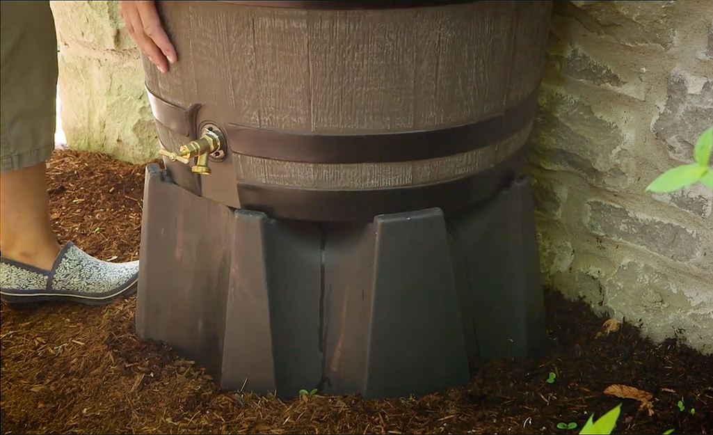 A rain barrel is placed on a raised stand to improve water flow.