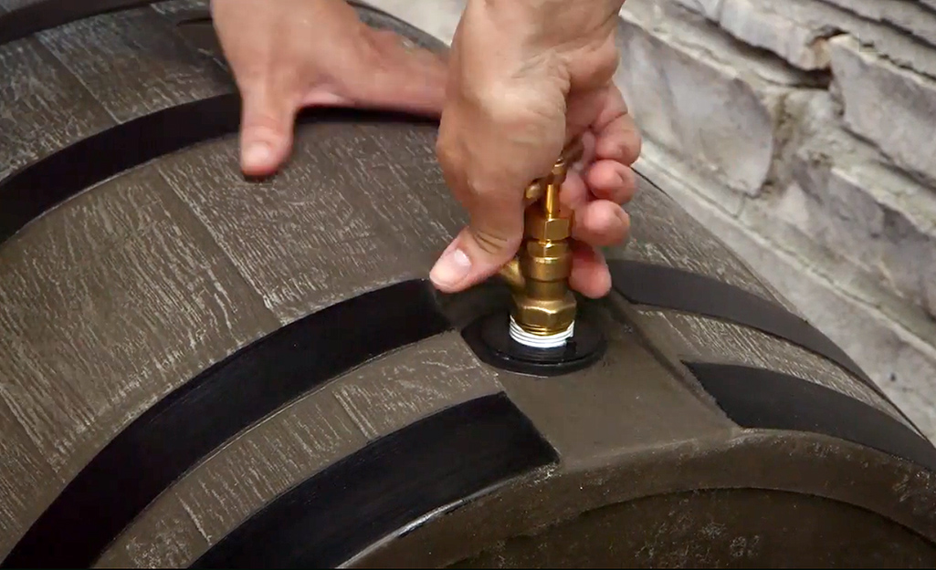 A person attaches a spigot near the base of a rain barrel.