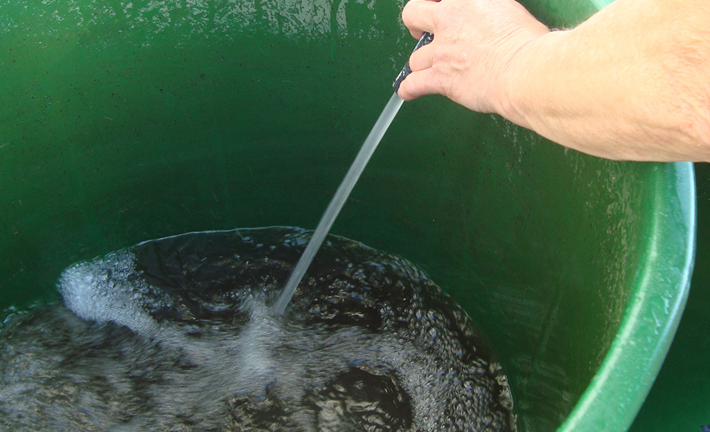 A person sprays water to clean the inside of a plastic barrel.